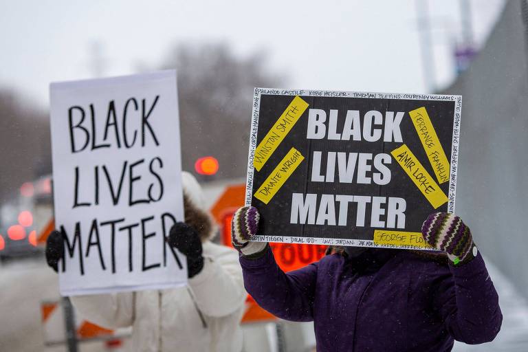 duas pessoas levantam cartazes com os dizeres "black lives matter" (vidas negras importam). elas usam roupas de frio e o cartaz tampa seus rostos
