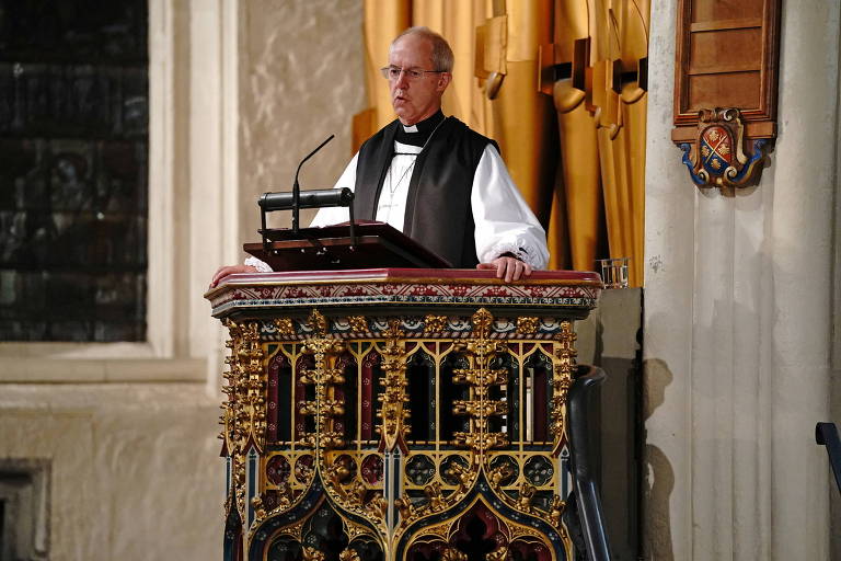 Em um púlpito de madeira feito de madeira com detalhes entalhados em dourando, o arcebispo de Canterbury, usando uma camisa branca e colete preto, faz um discurso 