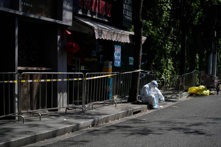 Funcionário da área da saúde com roupas de proteção contra a Covid descansa em rua deserta de Xangai, na China