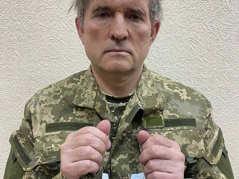 Viktor Medvedchuk posa de frente para a foto e mostra as mãos algemadas; ele usa um uniforme militar