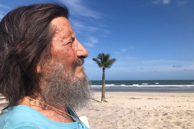 Imagem em primeiro plano mostra homem idoso de perfil em uma praia