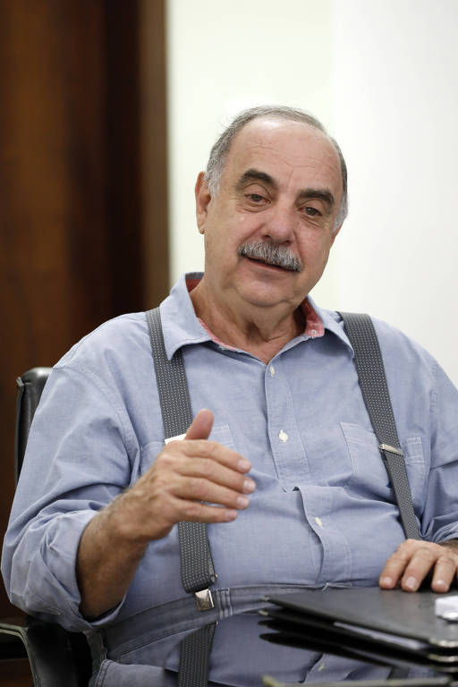 A foto mostra o novo prefeito de Belo Horizonte, Fuad Noman, sentado a uma mesa. Ele usa camisa azul e suspensório.