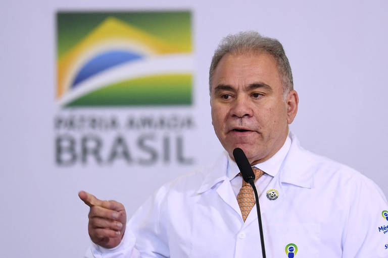 Marcelo Queiroga usa jaleco e fala com a marca do governo Bolsonaro ao fundo: Pátria amada Brasil
