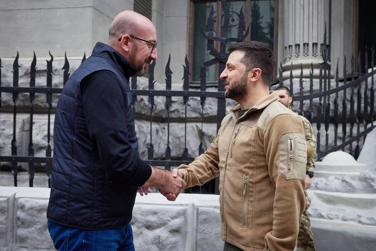 Charles Michel e Volodimir Zelenski apertam as mãos do lado de fora de um prédio do governo. 