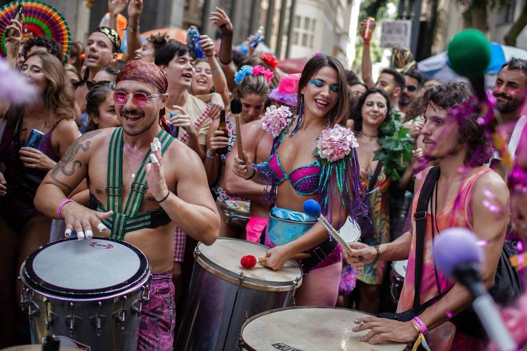 Pessoas vestindo roupas coloridas de Carnaval e usando adereços tocam tambores e dançam no Carnaval do Rio de Janeiro 