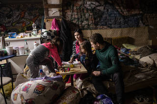 Parents Iliya, right and Lena try to entertain their two children, Valeria, 3, and Varvara, 6, in a basement shelter in the Ukrainian-held village of Avdiivka, just north of Russian-held Donetsk, on Wednesday, April 20, 2022. (Lynsey Addario/The New York Times)