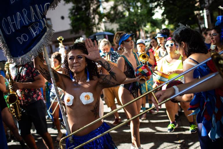 Mulher, com tapa-mamilos, carrega bandeira do bloco de carnaval