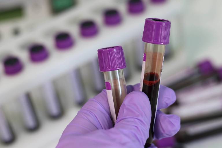Imagem de laboratório em que uma pessoa segura dois frascos com sangue