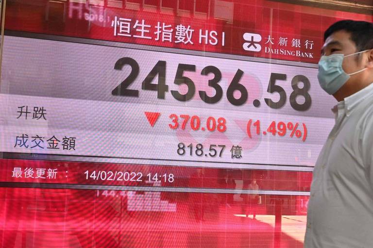 Pedestre diante de painel que mostra cotação do índice Hang Seng, o principal da Bolsa de Hong Kong