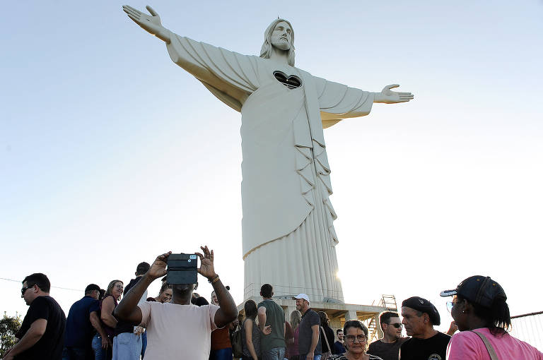 estátua de cristo com braços abertos como o do Cristo redentor no Rio cecado de público que tira fotos
