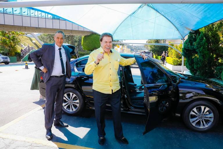 Silvio Santos saindo de um carro preto, e um homem atrás