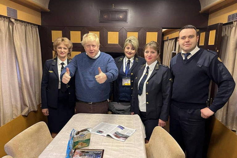 Boris Johnson aparece em uma cabine de trem, cercado por três funcionárias e um funcionários com uniforme da Ukrainian Railways
