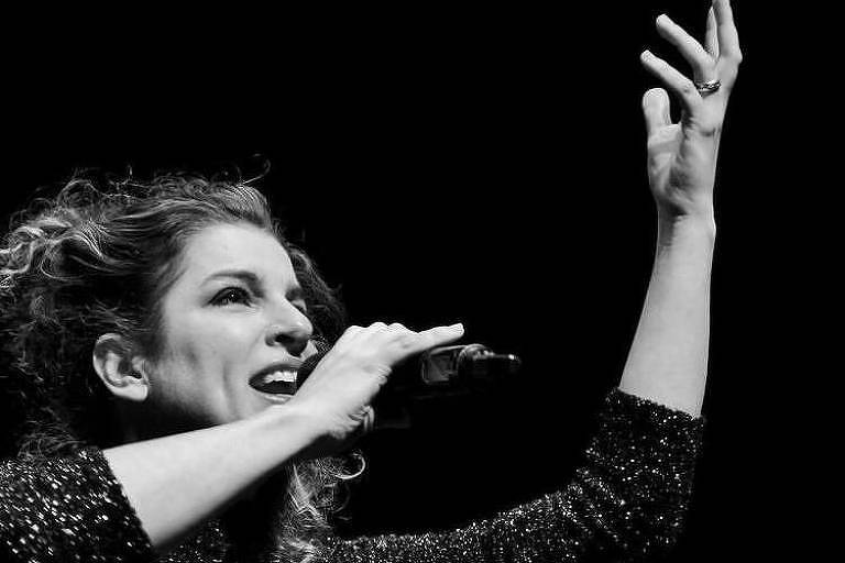 Em foto preto e branco a cantora e compositora Giana Viscardi aparece cantando com um microfone na mão direita
