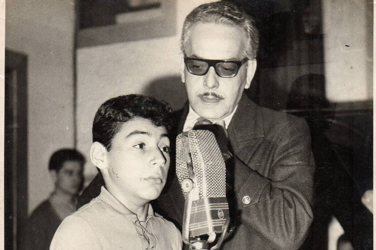 foto em preto e branco mostra garoto próximo a microfone com aotr Paulo Gracindo