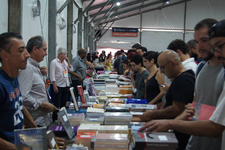 Centenas de pessoas estão reunidas em um salão repleto de estandes com livros
