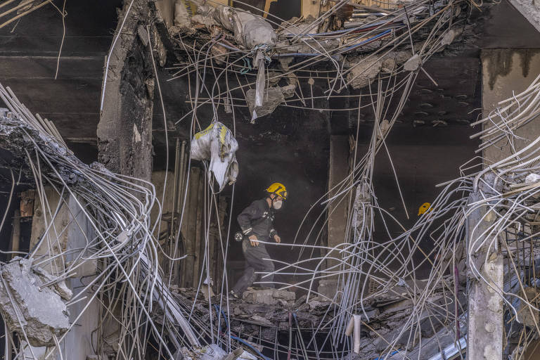 Trabalhador com uniforme e capacete aparece dentro de prédio em meio a muitos fios e estruturas de parede expostas