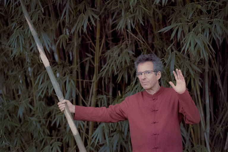 homem branco de cabelos grisalhos e óculos diante de plantas semelhantes a bambus