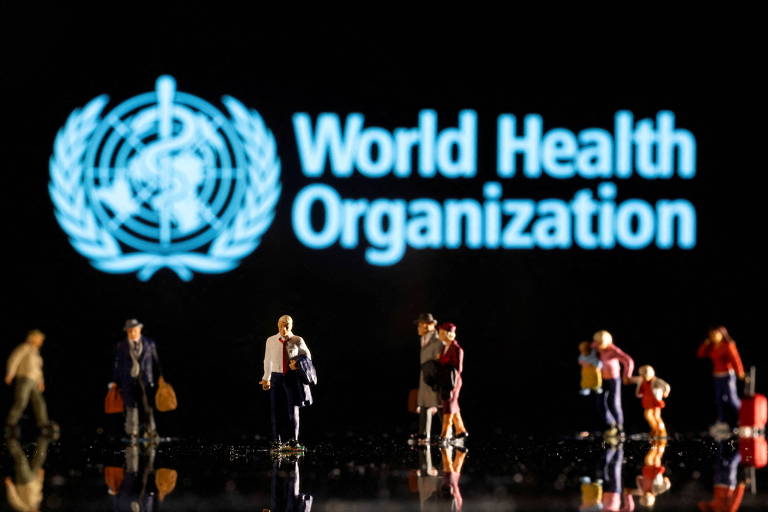 Pessoas são vistas em frente a painel da Organização Mundial da Saúde; entidade luta contra o tempo para identificar a causa dos casos de hepatite em crianças