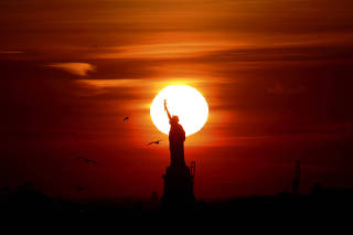 FILE PHOTO: The sun sets behind the Statue of Liberty in New York's Harbor as seen from the Brooklyn borough of New York