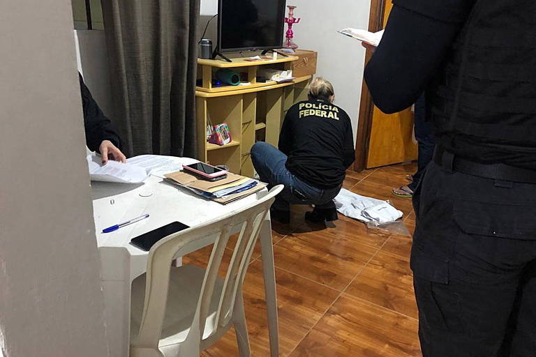 mulher sentada no chão de costas com camisa escrita Polícia Federal faz inspeção em cômodo