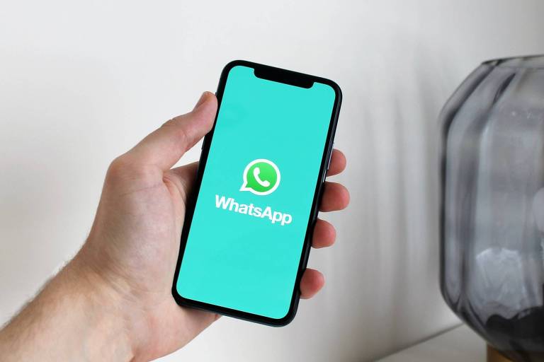 Foto mostra celular com tela verde e logo e nome do WhatsApp sendo segurado por uma mão