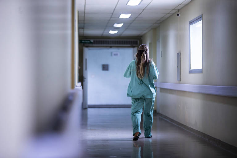 Imagem mostra médica vestida de azul andando por corredor de um hospital