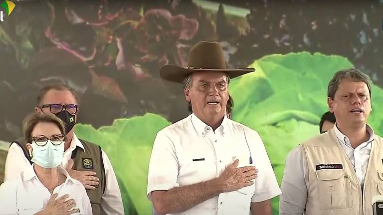 Bolsonaro com chapéu de vaqueiro e a mão direita no peito, durante execução do Hino Nacional
