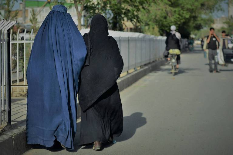 Mulheres vistas de costas andam em rua de Cabul, no Afeganistão; à esquerda, uma usa a burca, vestes azuis que cobrem completamente seu rosto, enquanto à direita a mulher usa um niqab, vestimenta que deixa apenas os olhos descobertos