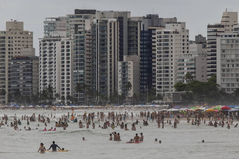 Imagem mostra praia lotada de turistas. Ao fundo, vários prédios compõem a paisagem.