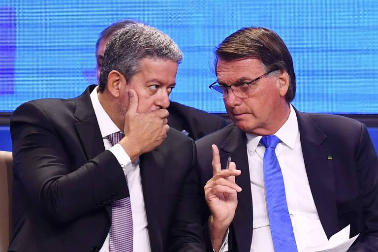 Homem cobre a boca ao conversar com Bolsonaro, que se inclina para ele apontando o indicador