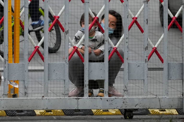 Moradora de Xangai e criança olham por meio de portão em área residencial, em meio ao lockdown devido à Covid