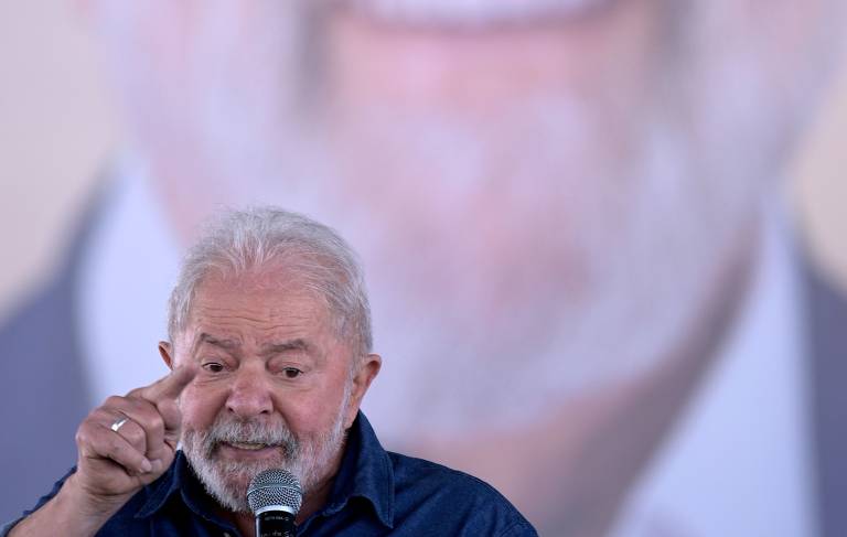Lula fala ao microfone, de frente; ao fundo, foto do queixo dele bem grande