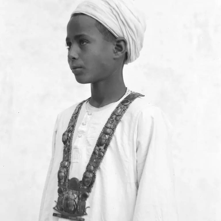 Um menino egípcio sem nome usa um pesado colar de jóias de um caixão dentro da tumba de Tutancâmon, unindo o Egito antigo e moderno