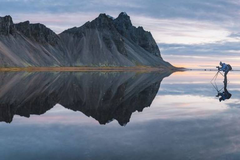 Imagem panorâmica mostra um homem com um tripé fotografando uma montanha