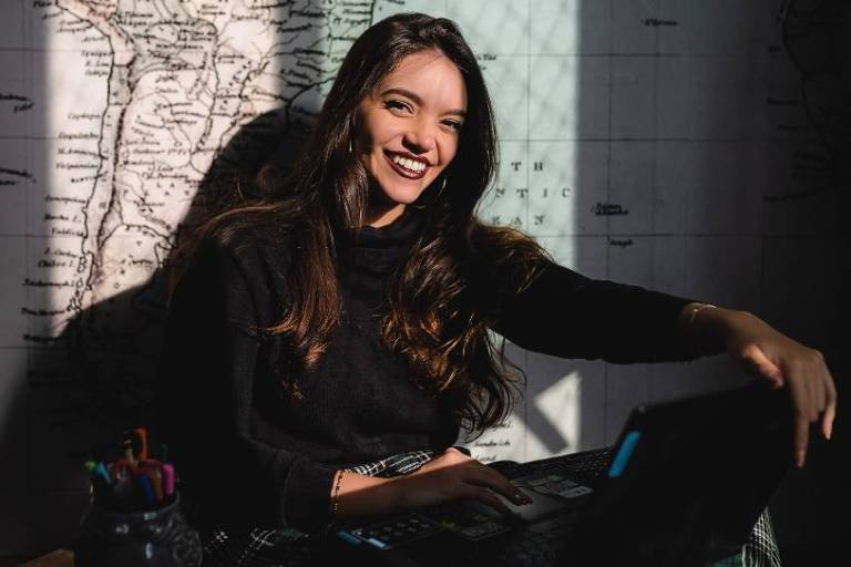 Retrato de Débora Aladim, 24, criadora de conteúdo para pré-vestibulandos. Na foto ela está sentada no chão, encostada em uma parede com um notebook no colo