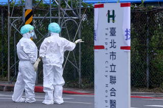 Medical workers in full PPE talk to each other at a newly open drive-through COVID test venue in Taipei