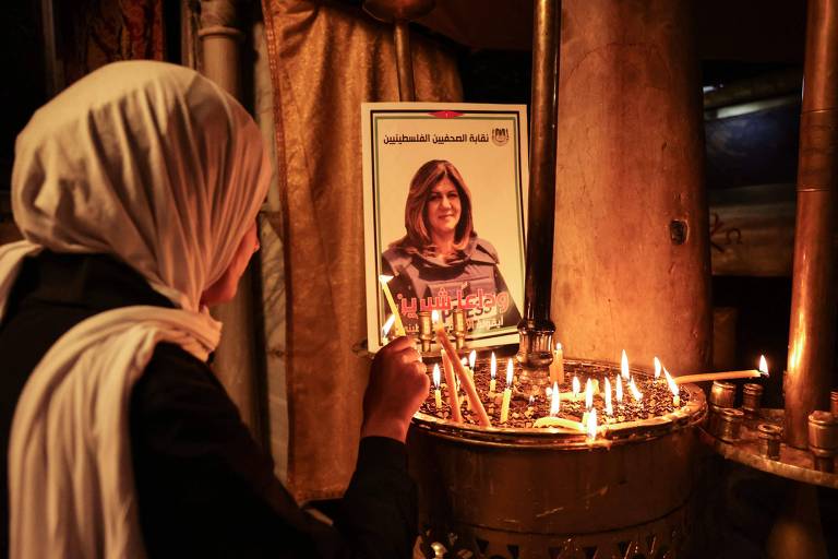 Mulher acende vela em frente a fotografia da jornalista da Al-Jazeera Shireen Abu Akleh, morta enquanto cobria ação do Exército israelense em Jenin, na Cisjordânia
