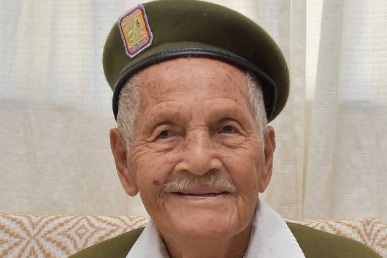 Imagem em primeiro plano mostra homem idoso posando para foto sorrindo e usando uniforme do Exército