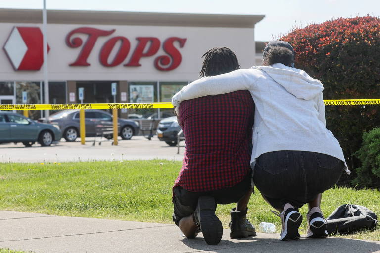 Duas pessoas são vistas agachadas e abraçadas próximo a cordão de isolamento na área do supermercado onde ocorreu tiroteio na noite deste sábado (14) 