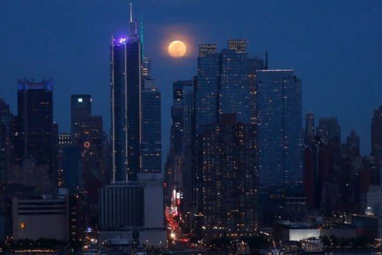 Imagem panorâmica mostra a cidade de Nova York e a lua no meio de prédios