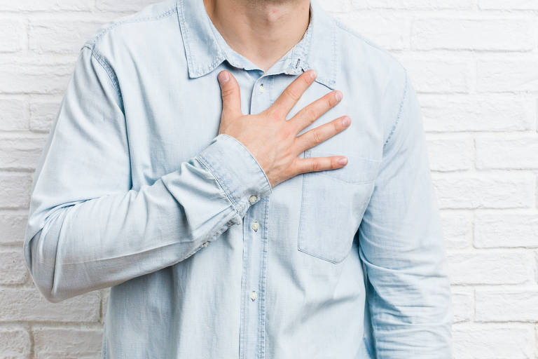 Imagem em primeiro plano mostra homem de camisa social com a mão espalmada no peito