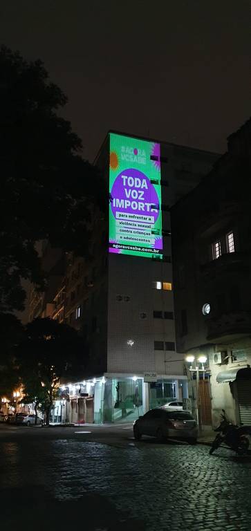 Imagem de um prédio à noite com a projeção visual em um edifício com a frase da campanha Agora Você Sabe