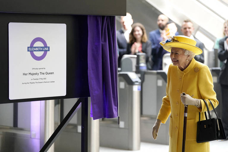A rainha Elizabeth 2ª ao lado da placa da linha que leva o nome dela no metrô de Londres