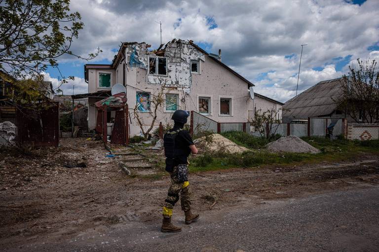 Soldado das forças ucranianas passa em frente a casa destruída na vila de Rus'ka Lozova