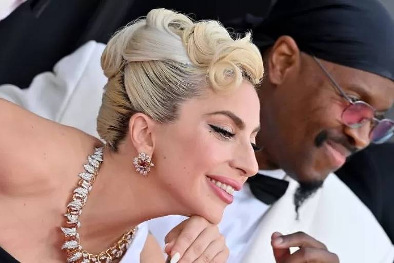 Imagem em primeiro plano mostra Lady Gaga posando para foto ao lado de um homem negro