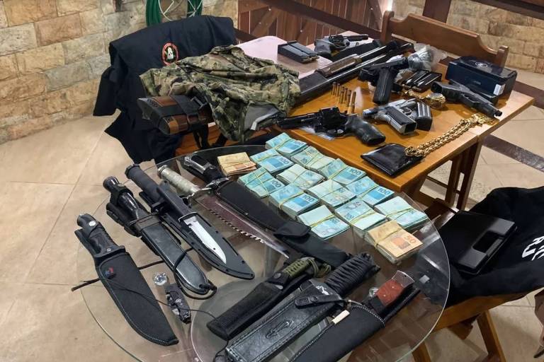 Maços de dinheiro, pistolas e facas exibidos sobre a mesa