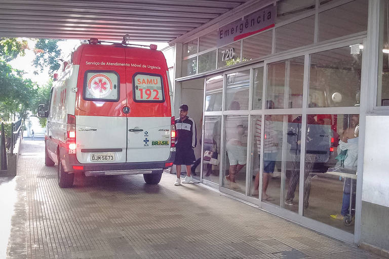 A imagem mostra a entrada de um pronto-socorro com uma ambulância do Samu, nas cores branca e vermelha na porta
