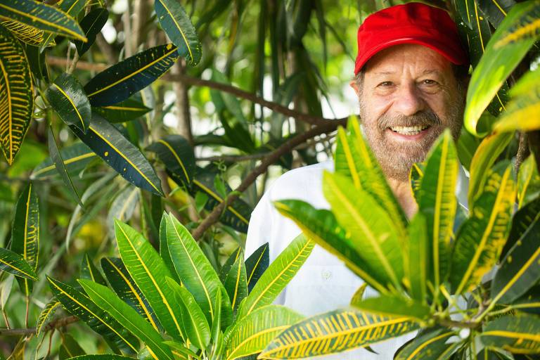 Em foto colorida, o cantor e compositor João Bosco posa sorrindo entre plantas