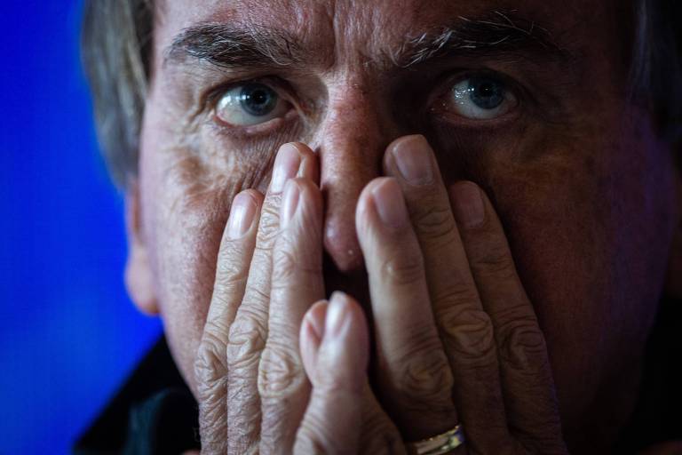 Jair Bolsonaro coloca as duas mãos no rosto, deixando apenas os olhos de fora