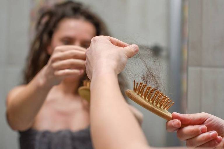Mulher observa queda de cabelo em escova